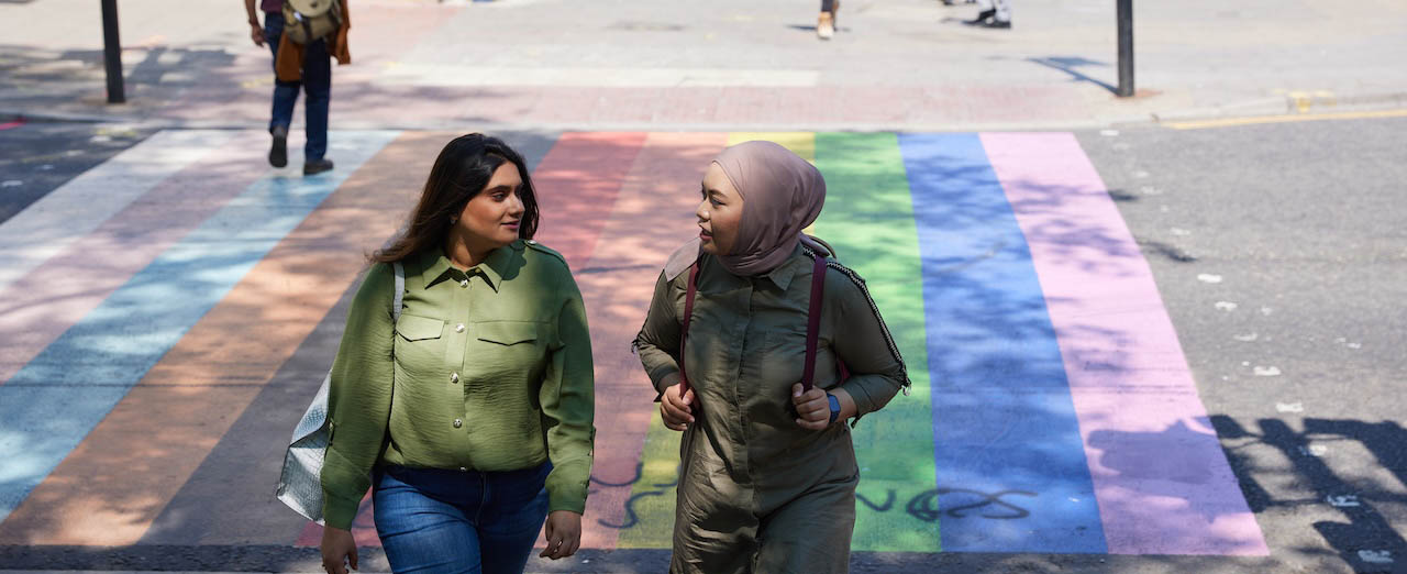 international students crossing the road at a pedestrian crossing painted with the trans and pride flags